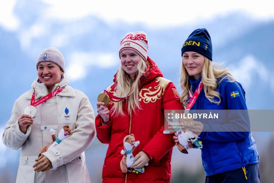 Серебряная медалистка Орели Ришар из Франции, золотая медалистка Варвара Ворончихина из России и бронзовая медалистка Эбба Аршё из Швеции на пьедестале почета на церемонии награждения в супергиганте среди женщин в третий день зимних Паралимпийских игр Милан-Кортина-2026, 9 марта 2026 года. Фото: Маxim Tore/Bildbyran