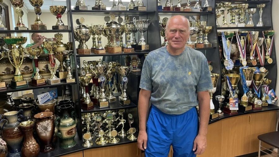 Пётр Ремпель на фоне спортивных трофеев в кабинете председателя районного спорткомитета