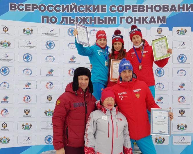 Призовой подиум масс-старта в Тюмени. Яна Кирпиченко на пьедестале в центре, её тренер Артемий Гельманов в первом ряду справа. Фото: ФЛГР